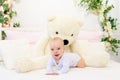 A small baby girl 6 months old is lying on a white bed at home with a large Teddy bear Royalty Free Stock Photo