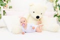 A small baby girl 6 months old is lying on a white bed at home with a large Teddy bear and sucking on a pacifier Royalty Free Stock Photo