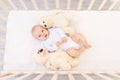 A small baby girl 6 months old in a white bodysuit is lying on her back in a child`s bed with soft toys bears Royalty Free Stock Photo