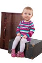 Small baby girl sitting on the old wooden box with a suitcase, w Royalty Free Stock Photo