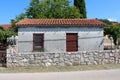 Small backyard unfinished outdoor storage structure with window and wooden door surrounded with traditional stone wall and trees