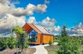 Small barnhouse on a plot with green trees under a cloudy sky. Modern small housing Royalty Free Stock Photo