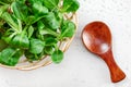 Small basket with corn salad Valerianella locusta, tiny wooden spoon next to it on white board, photo from above. Healthy green