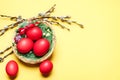 Small basket with red Easter eggs, swelled willow buds on yellow background, copy space