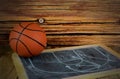 A small basketball and a chalkboard showing a classic pick and roll play, all on a wooden background.