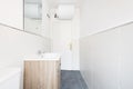 Small bathroom with a white porcelain sink integrated into a wooden cabinet with drawers, a frameless mirror and a water heater Royalty Free Stock Photo