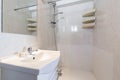 Small bathroom with a white porcelain sink on a wooden cabinet and a frameless square mirror, a plastic shelf in one corner and a Royalty Free Stock Photo