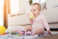 A small beautiful baby sits on the floor and plays with bright, flowery toys.