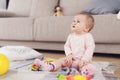 A small beautiful baby sits on the floor and plays with bright, flowery toys.