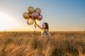 Small beautiful girl with balloons in the gold wheat field Royalty Free Stock Photo