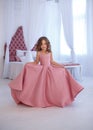 A small, beautiful girl in a luxurious pink dress, is gaily circling in a white room.