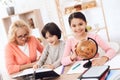 Small beautiful girl is studying globe next to elderly woman who looks at book with little boy. Royalty Free Stock Photo