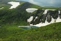 A small beautiful lake at the foot of a high mountain with the remains of snow on the slopes overgrown with tall pines Royalty Free Stock Photo