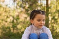 A small beautiful smiling schoolgirl on a natural background in a turtleneck sweater and jeans sits on the ground hugging her legs Royalty Free Stock Photo