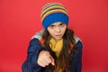 Small beauty red background. little girl puffer jacket and knitted hat. care yourself in cold weather. kid pointing