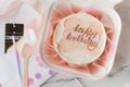 Small birthday cake in a white gift box with a spoon and candle. Trendy Korean style bento cake with Happy birthday inscription