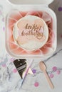 Small birthday cake in a white gift box with a spoon and candle. Trendy Korean style bento cake with Happy birthday inscription