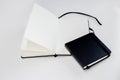 Small black closed and large open notebooks with blank white pages and ribbon bookmark lie unfold on white background