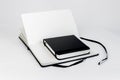 Small black closed notepad on large open notebook with blank white pages and ribbon bookmark lie unfold on white background