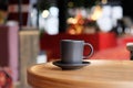 A small black coffee cup on a saucer on a wooden table. Coffee in a cafe on the background of blurred background Royalty Free Stock Photo