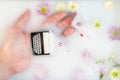 Small black typewriter in woman hand lay in milk water with tender flowers around. Top view, flat lay. Spring concept