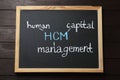 Small blackboard with abbreviation HCM Human Capital Management on wooden background, top view