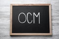 Small blackboard with abbreviation OCM Organizational Change Management on white wooden background, top view