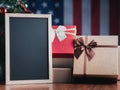 Small blackboard and gift boxes on wooden table with a Christmas tree and American flag in the background. Space for text Royalty Free Stock Photo