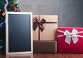 Small blackboard and gift boxes on wooden table with a Christmas tree and vintage wall background. Space for text. Concept of Royalty Free Stock Photo