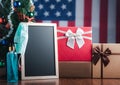 Small blackboard, mask, alcohol gel, and gift boxes on wooden table with a Christmas tree and American flag in the background. Royalty Free Stock Photo