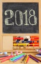 Small blackboard in wooden abacus frame and hand written 2018 new year greeting on it. Scattered stationery, colorful pencils, ch Royalty Free Stock Photo