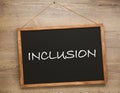 Small blackboard with word INCLUSION hanging on wooden wall Royalty Free Stock Photo