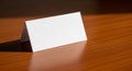 A small, blank, folded white card rests on a polished wooden surface. The card is tent- Royalty Free Stock Photo