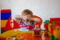 A small blond boy at home sits at an children's table among plastic toys and hides covering his face with his hands Royalty Free Stock Photo