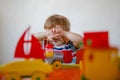 A small blond boy at home sits at an children's table among plastic toys and hides covering his face with his hands Royalty Free Stock Photo