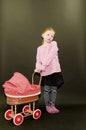 Small blond girl and dolls pram on black background. Little girl stands on black background.