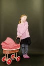 Small blond girl and dolls pram on black background. Little girl stands on black background.