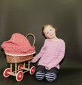 Small blond girl and dolls pram on black background. Little girl sits on black background.