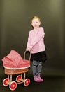 Small blond girl and dolls pram on black background. Little girl stands on black background.