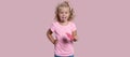 Small blond girl holds lollipop and shows a tong isolated over pink background