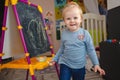 A small blonde smiling girl at home in the game room near the blackboard with chalk in her hands Royalty Free Stock Photo