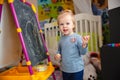 A small blonde smiling girl at home in the game room near the blackboard with chalk in her hands Royalty Free Stock Photo