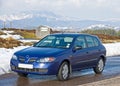 Small blue car in a snowy landscape.