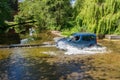 Small Blue Van Driving Across a Shallow River.