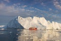 A small boat among icebergs. Sailboat cruising among floating icebergs in Disko Bay glacier during midnight sun Greenland