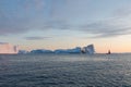 A small boat among icebergs. Sailboat cruising among floating icebergs in Disko Bay glacier during midnight sun Greenland
