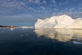 A small boat among icebergs. Sailboat cruising among floating icebergs in Disko Bay glacier during midnight sun Greenland