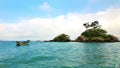 A small boat in the sea in front of a beautiful island with lots of rocks and vegetation Royalty Free Stock Photo