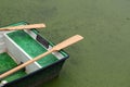 A small boat with two oars on a pond with duckweed