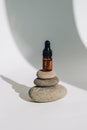 Small bottle of serum on stack of basalt stones on white background. Trendy shadows. Beauty pipette dropper on pyramid of pebbles Royalty Free Stock Photo